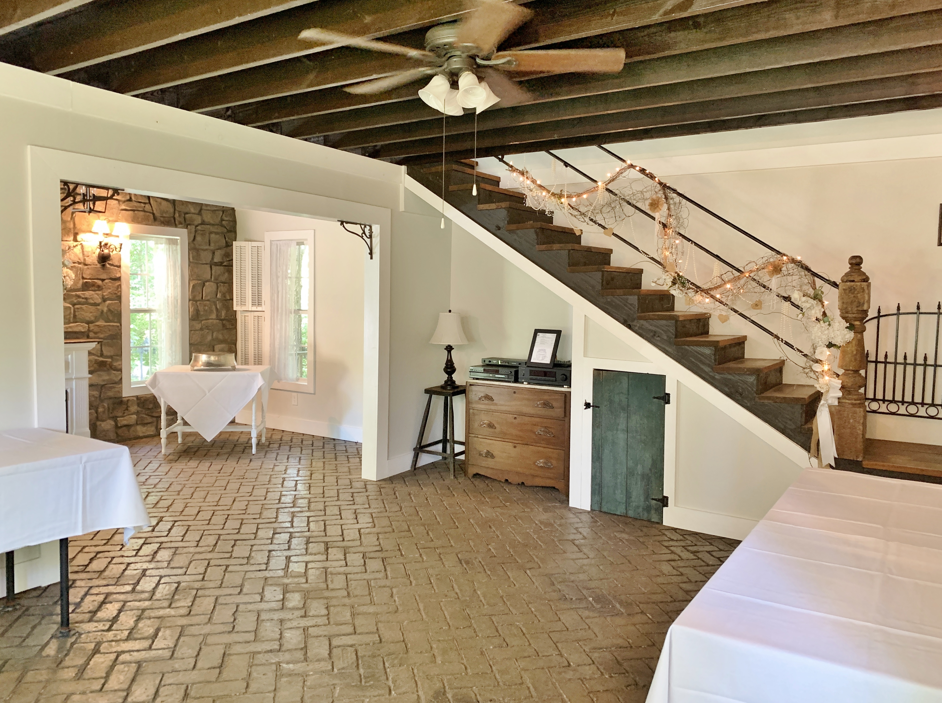 Interior photo of cottage showing stairs, buffet tables, cake table, and brick flooring.