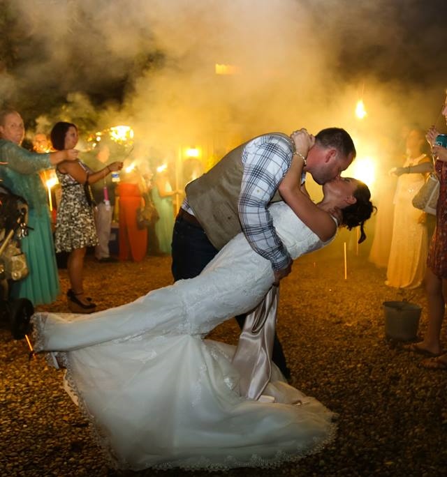 Groom dips bride while guests illuminate with sparklers.