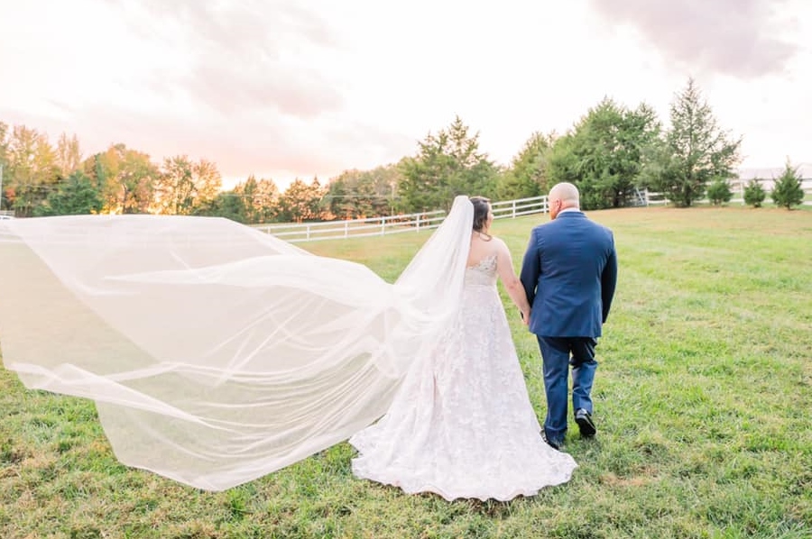 Long veil blows in the breeze while bride and groom walk.