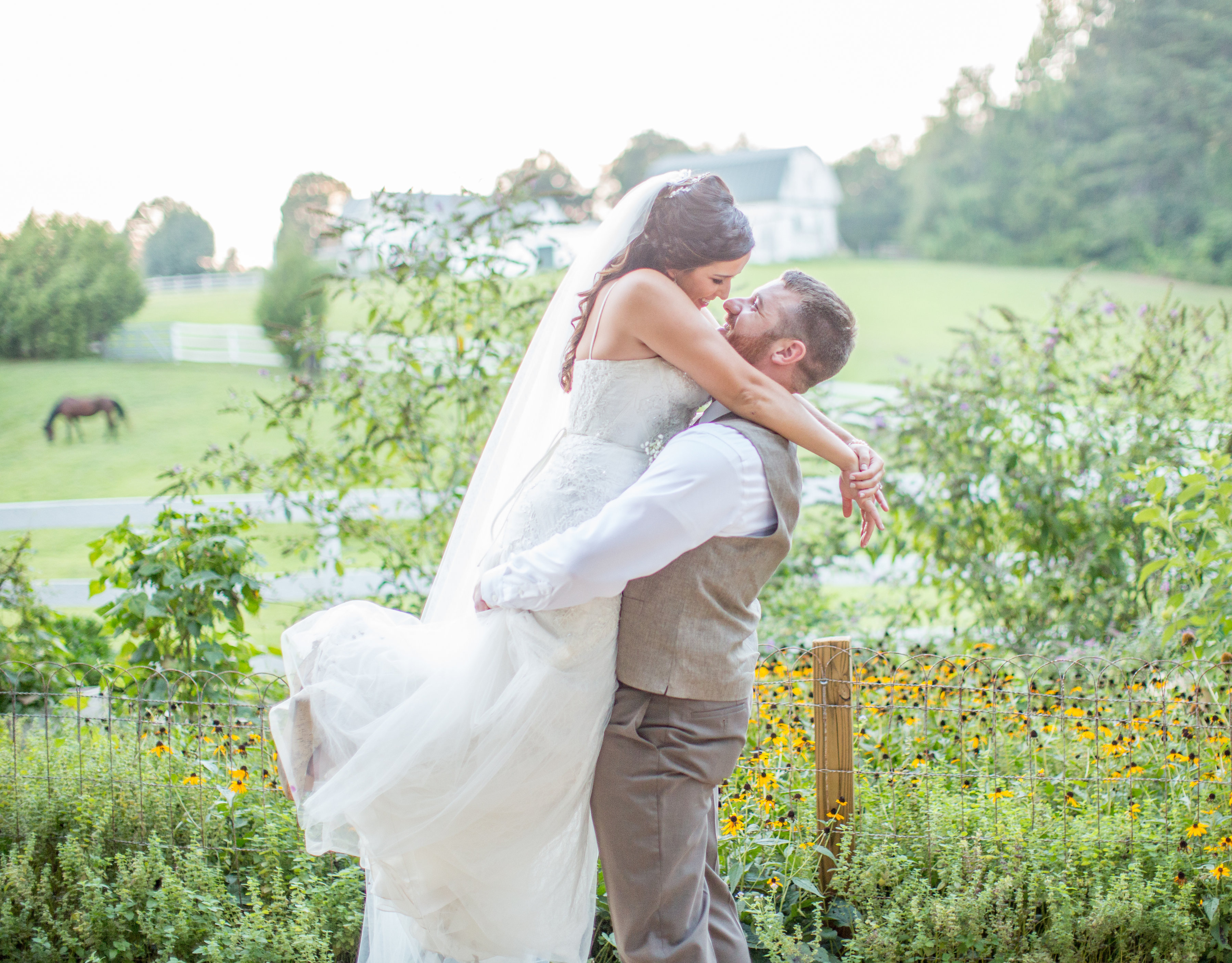 Standing in front of the flowers, groom lifts bride.